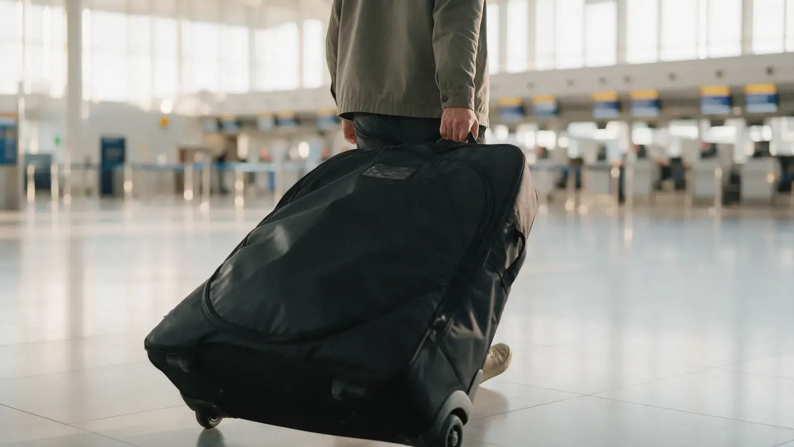 Person zieht eine schwarze gepolsterte Radtasche auf Rollen durch eine helle Abflughalle