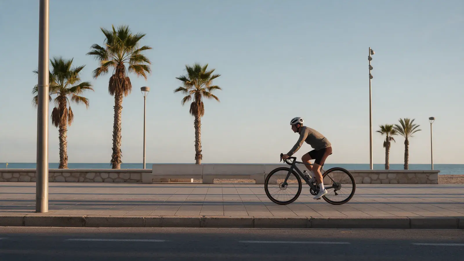 Rennradfahrer auf einer Strandpromenade mit Palmen und Meer bei Valencia