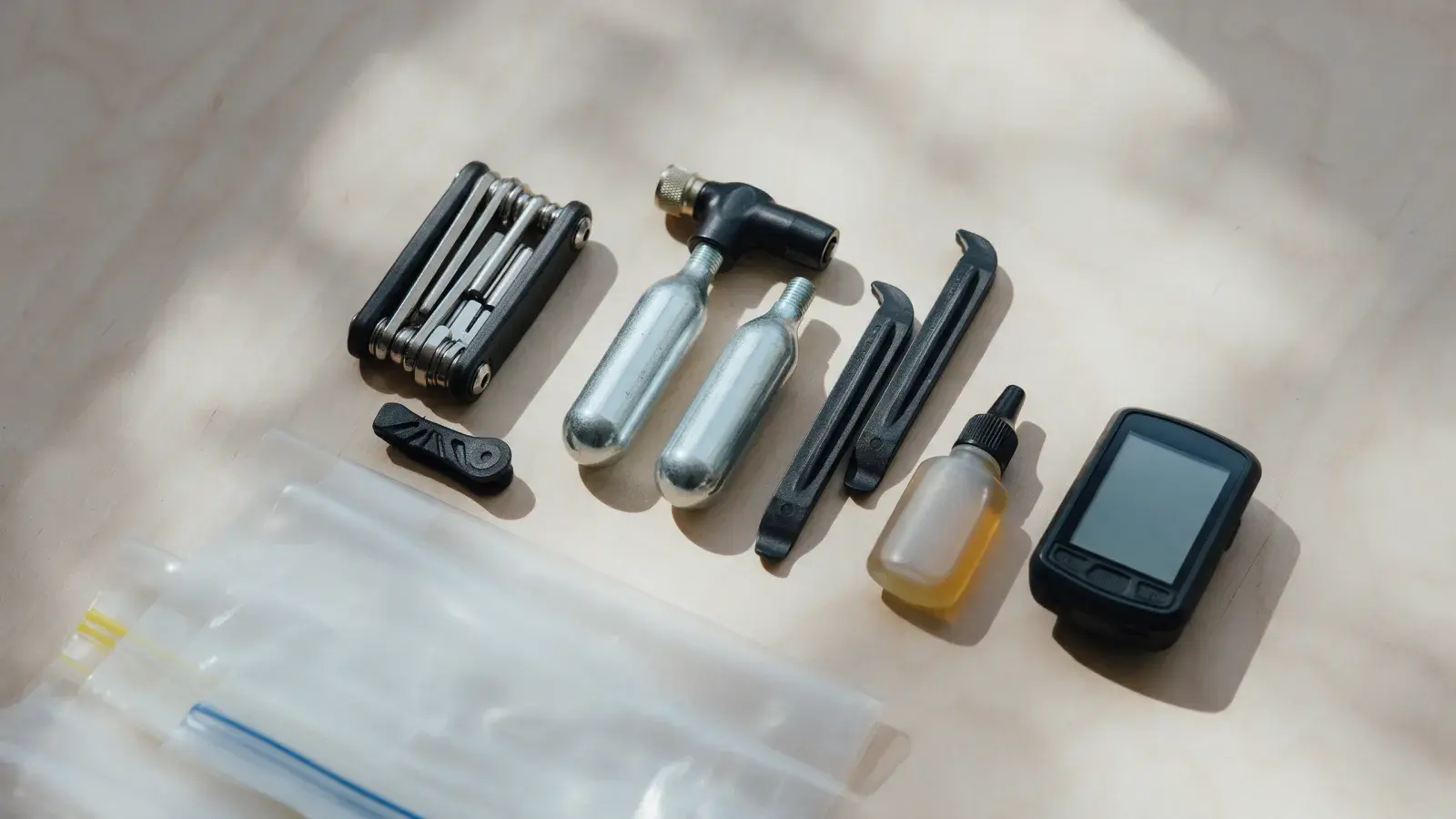 Multitool, zwei CO2-Kartuschen, Reifenheber, Kettenöl und Radcomputer auf hellem Holz